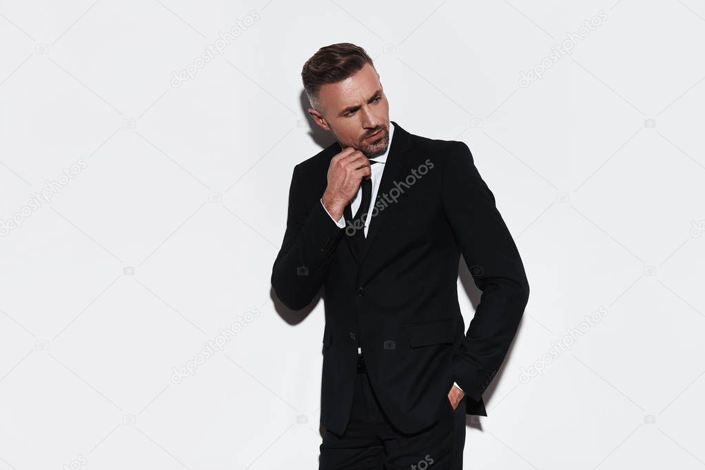 Thinking about solution man in full suit keeping hand in pocket and looking away while standing against white background