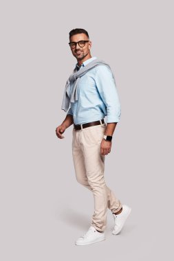 gülümseyen ve gri arka plan üzerinde yürürken kameraya bakarak şık yakışıklı genç adam