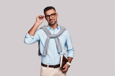 Beyaz adam ayakta beyaz arka planı ve günlük ders kitabı tutarak, gözlük yenilemesi ve kameraya gülümseyen 