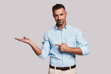 Eller kopya alanı için işaret ve kamera gri arka plan karşı dururken bakarak yakışıklı delikanlı
