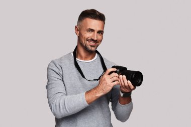 dijital kamera tutarak ve gri arka plan üzerinde duran gülümseyen yakışıklı adam