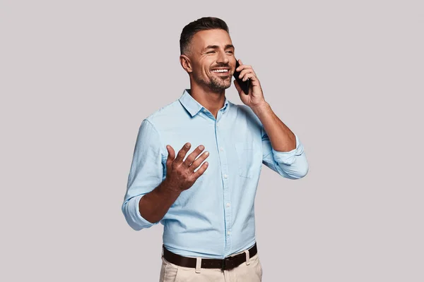 電話で話していると灰色の背景に対して立っている笑顔のスマートのカジュアルな服装で格好良い若い男 — ストック写真