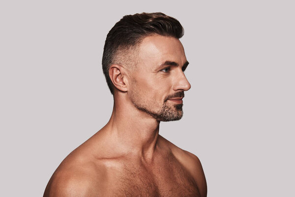 красивый молодой человек смотрит в сторону и улыбается стоя на сером фоне
