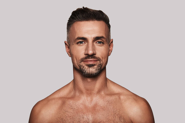 без рубашки и красивый мужчина смотрит в камеру и улыбается стоя на сером фоне

