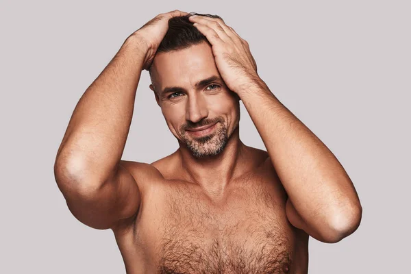 魅力的な上半身裸の男の髪に手を維持して灰色の背景に対して立っている笑顔 — ストック写真