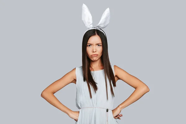 愤怒的年轻亚洲妇女在兔子耳朵看着相机 而站在灰色的背景 — 图库照片