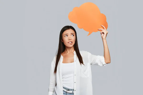 thinking young Asian woman holding orange speech bubble for copy space