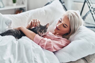 Onu kedi ile oynarken ve evde yatakta yatan süre gülümseyen çekici genç kadın                