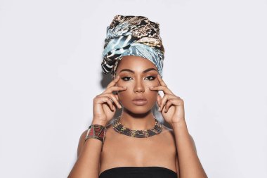 Doğal güzelliğiyle parlıyor. Çekici Afrikalı kadın kamera gri arka plan karşı dururken bakarak türban