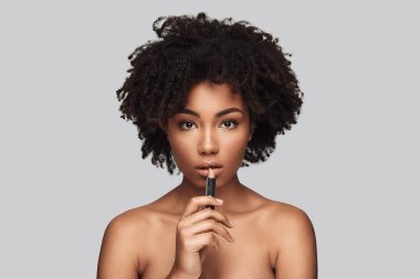 Utting biraz ruj. Çekici genç Afrikalı kadın kamera gri arka plan karşı dururken bakarak