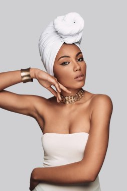 Onun tarzı kendine güvenen. Çekici Afrikalı kadın kamera gri arka plan karşı dururken bakarak türban