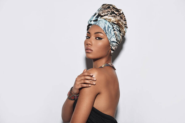 Simply stunning. Attractive young African woman in turban looking at camera while standing against grey background
