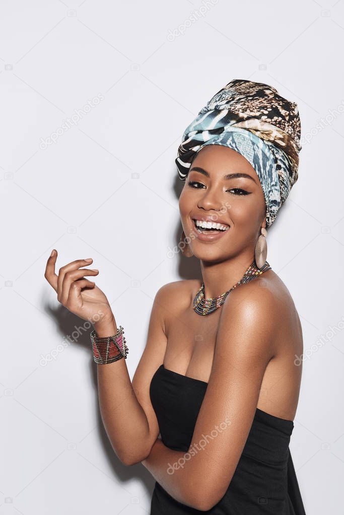 African beauty. Attractive young African woman in turban looking at camera and smiling while standing against grey background