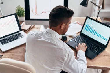Arkadan görünüm Office masada dizüstü bilgisayarlar ve bilgisayar kullanarak iş adamı 