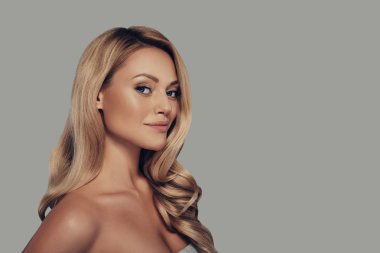 uzun kıvırcık sarı saçlı gülen ve kamera gri arka plan karşı dururken bakarak çekici genç kadın