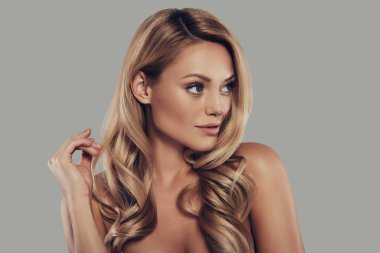 gülümseyen ve uzak duran gri arka planı arıyorum uzun kıvırcık sarışın çekici genç kadın