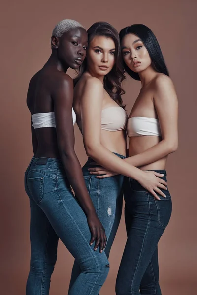 Три Привлекательные Молодые Женщины Смотрят Камеру Стоя Коричневом Фоне Бюстгальтерах — стоковое фото