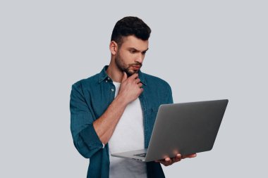 dizüstü bilgisayar kullanmak ve çene duran gri arka plan üzerinde el tutmak düşünceli genç adam