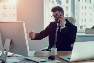 İş ayrıntıları, yakışıklı genç adam telefonda konuşurken ve monitöre ofiste otururken gösteren resmi kıyafeti içinde tartışıyor