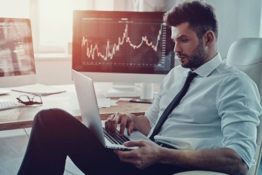 Yeni proje, düşünceli genç iş adamı ofiste otururken dizüstü kullanarak resmi kıyafeti geliştirme