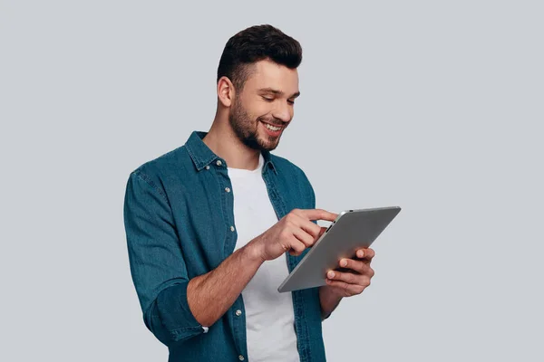 魅力的な若い男彼のデジタル タブレットを使用して 灰色の背景に対して立っている笑顔 — ストック写真