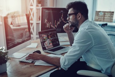 düşünceli genç iş adamı ofiste otururken bilgisayar kullanarak verileri analiz resmi kıyafeti