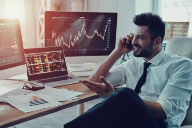 Akıllı telefonda konuşurken ve ofiste otururken gülümseyen resmi kıyafeti içinde genç işadamı