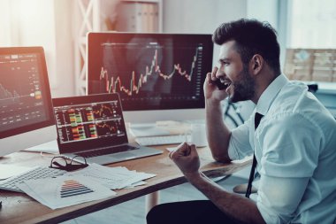 Akıllı telefonda konuşurken ve ofiste otururken gülümseyen resmi kıyafeti içinde genç işadamı