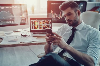 düşünceli genç iş adamı ofiste otururken akıllı telefonunu kullanarak resmi kıyafeti