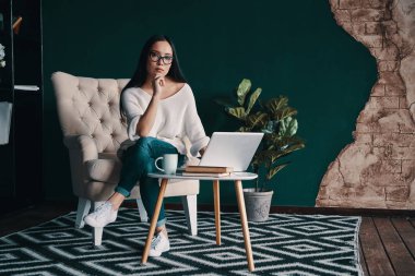 Akıllı ve kendinden emin. Güzel genç kadın koltukta otururken kameraya bakıyor