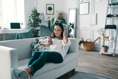 İnternette sörf yapıyorum. Evde vakit geçirirken akıllı telefonunu kullanan güzel genç kadın