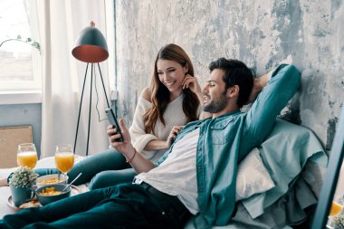 Kahvaltı, portakal suyu ve tarama cep telefonu ile yatakta Kafkas genç çift harcama zamanı  