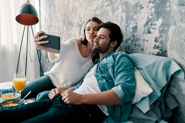 beautiful young couple taking selfie on mobile and smiling while spending time in bed at home