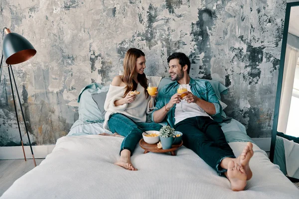 Lazy morning, Beautiful young couple having breakfast with orange juice while spending time in bed at home