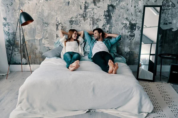 美丽的年轻夫妇在爱躺在床上在家里的手背后的头 — 图库照片