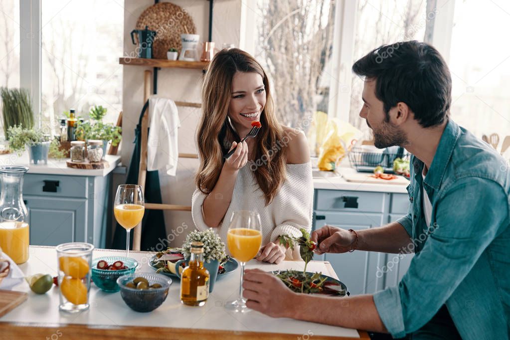 beautiful young couple enjoying healthy breakfast while sitting in kitchen at home