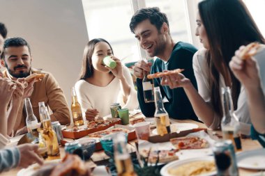 Sadece rahatlıyor. Gündelik giyimli bir grup genç, içeride akşam yemeği partisi verirken pizza yiyip gülümsüyor