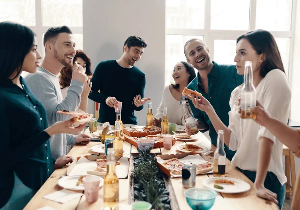 很棒的派对一群穿着休闲装的年轻人在室内举行晚宴时吃披萨并微笑 — 图库照片