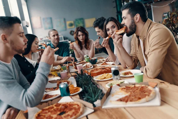 很棒的食物和公司 一群穿着休闲装的年轻人在室内举行晚宴时吃披萨并微笑 — 图库照片