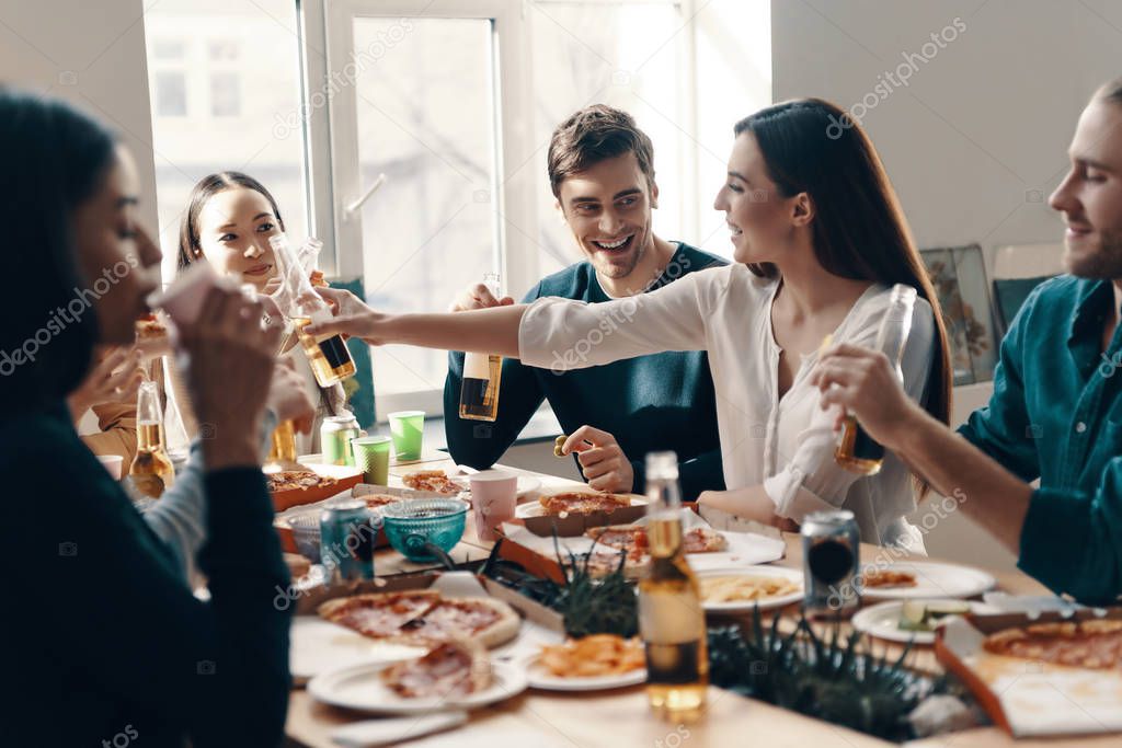 Having fun. Group of young people in casual wear eating pizza and smiling while having a dinner party indoors
