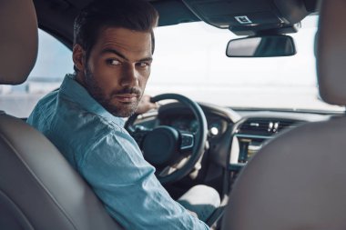 Gitmeye hazır mısın? Bir durum araba sürerken omuz üzerinden bakan akıllı rahat giyim genç adamın arka görünümü