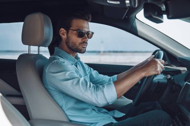 Yeni arabasını kullanıyor. Bir durum araba sürerken uzak bakıyor akıllı rahat giyim yakışıklı genç adam