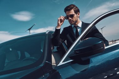 Lüks yaşam tarzları. İş dünyasında yakışıklı genç adam arabasının yanında dururken güneş gözlüğü ayarlıyor           