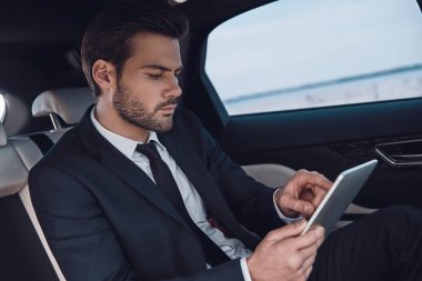 İş yerinde konsantre oldu. Arabada otururken dijital tablet kullanarak çalışan tam takım elbiseyakışıklı genç adam  