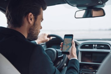 Neredeyim ben? Takım elbiseli genç adam araba sürerken haritayı kontrol etmek için akıllı telefon kullanıyor.        