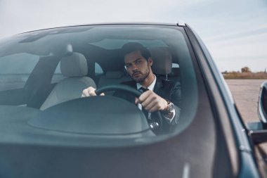 Dikkatli sürücü. Tam takım elbiseli yakışıklı genç adam bir araba sürerken düz görünümlü