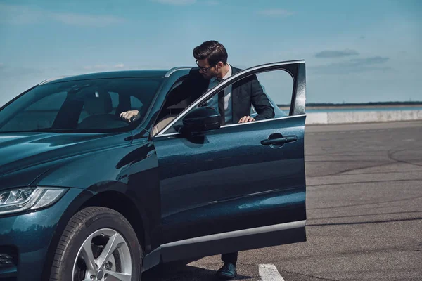 Yepyeni bir araba. Yakışıklı genç işadamı dışarıda dururken arabasına giriyor