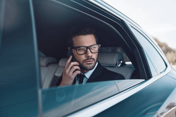 Discussing business details. Thoughtful young businessman talking on the phone while sitting in the car