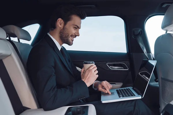 成功驱动 英俊的年轻人在全西装工作使用笔记本电脑 而坐在车里 — 图库照片