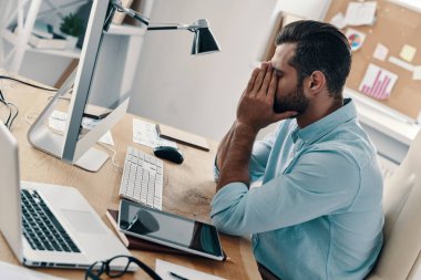 Ofiste otururken elleri yüz tutmak akıllı rahat giyim yorgun genç adam üst görünümü         